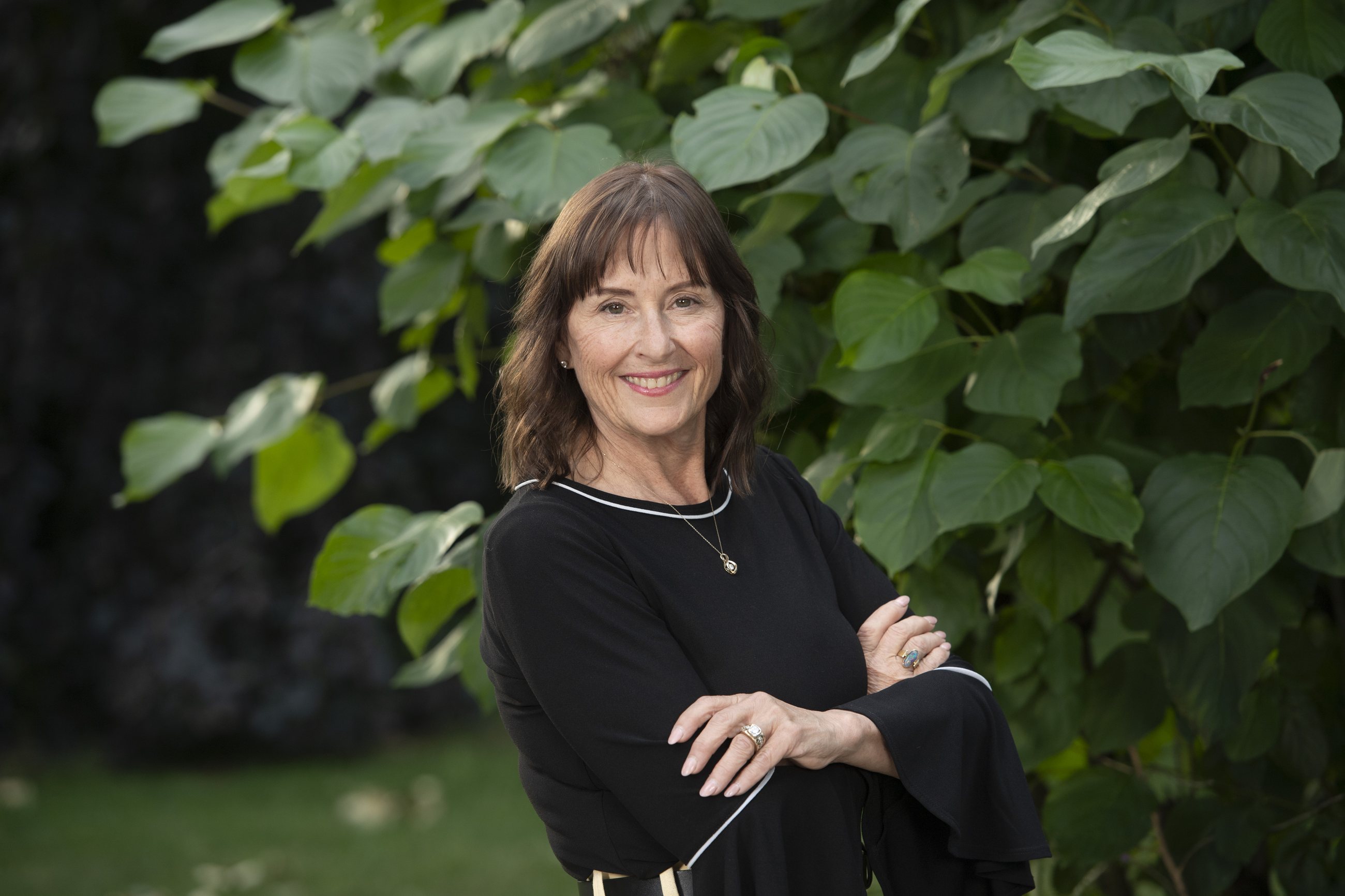 Mayor Meghan Lahti, smiling with her arms crossed in front of greenery