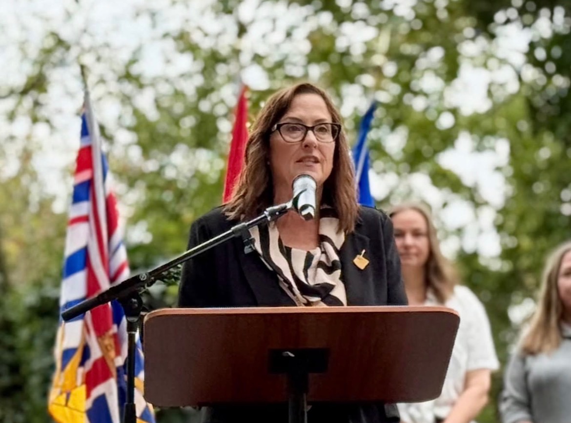 Meghan Lahti delivering a speech at a podium with flags behind her